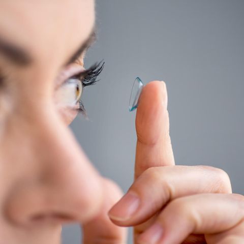 Eine Frau setzt sich eine Kontaktlinse ins linke Auge