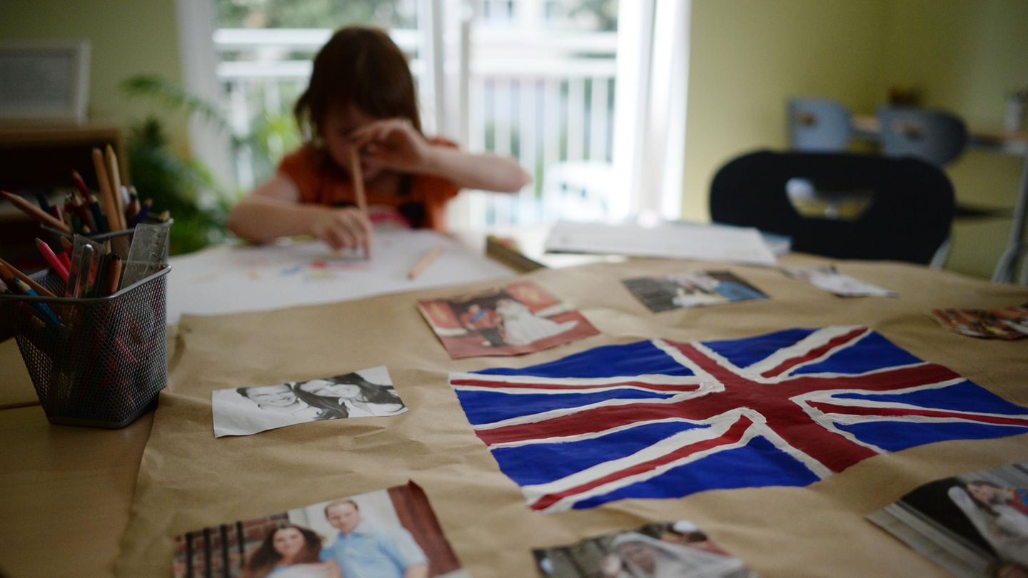 Ein kleines Mädchen sitzt am Tisch und malt. Vor ihr liegt die britische Flagge