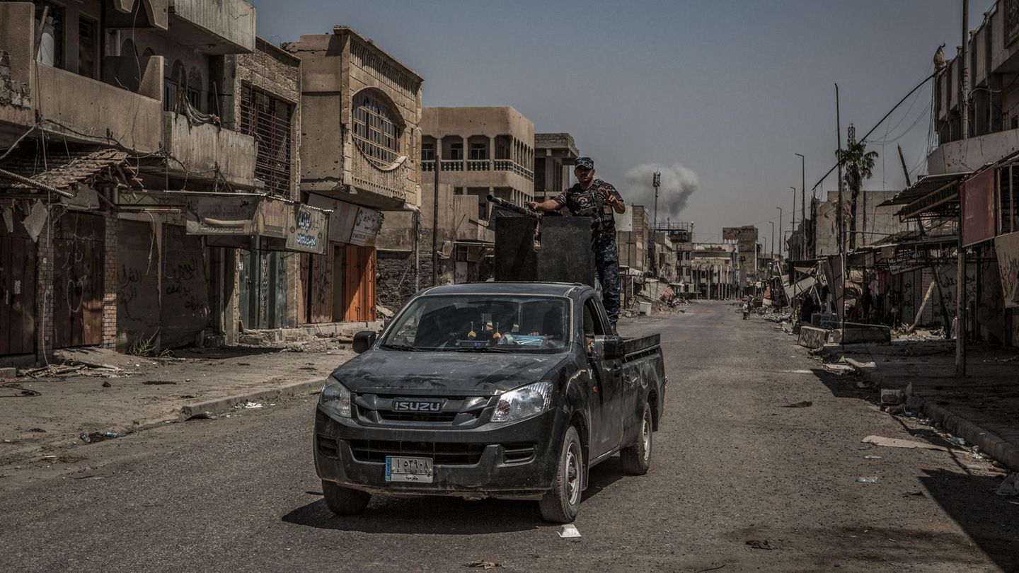 Eine Rauchsäule steigt in Mossul (Irak) hinter einen Polizeifahrzeug auf