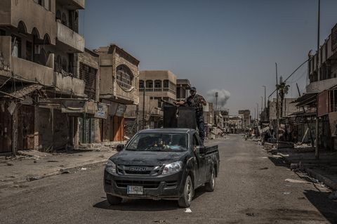 Eine Rauchsäule steigt in Mossul (Irak) hinter einen Polizeifahrzeug auf