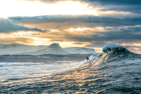 "Der Surfer Nic von Rupp surft eine winterliche Welle vor den schneebedeckten Bergen bei Bundoran, Irland."