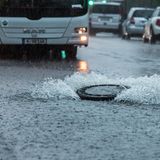 Der Deckel eines Gullys wird auf einer überfluteten Straße in Köln vom Wasserdruck hochgehoben