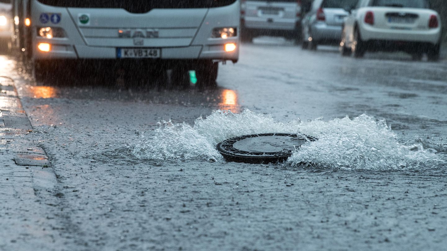 Der Deckel eines Gullys wird auf einer überfluteten Straße in Köln vom Wasserdruck hochgehoben