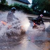 Zwei Motorradfahrer bahnen sich ihren Weg über eine überflutete Straße in der Region Hannover (Niedersachsen).