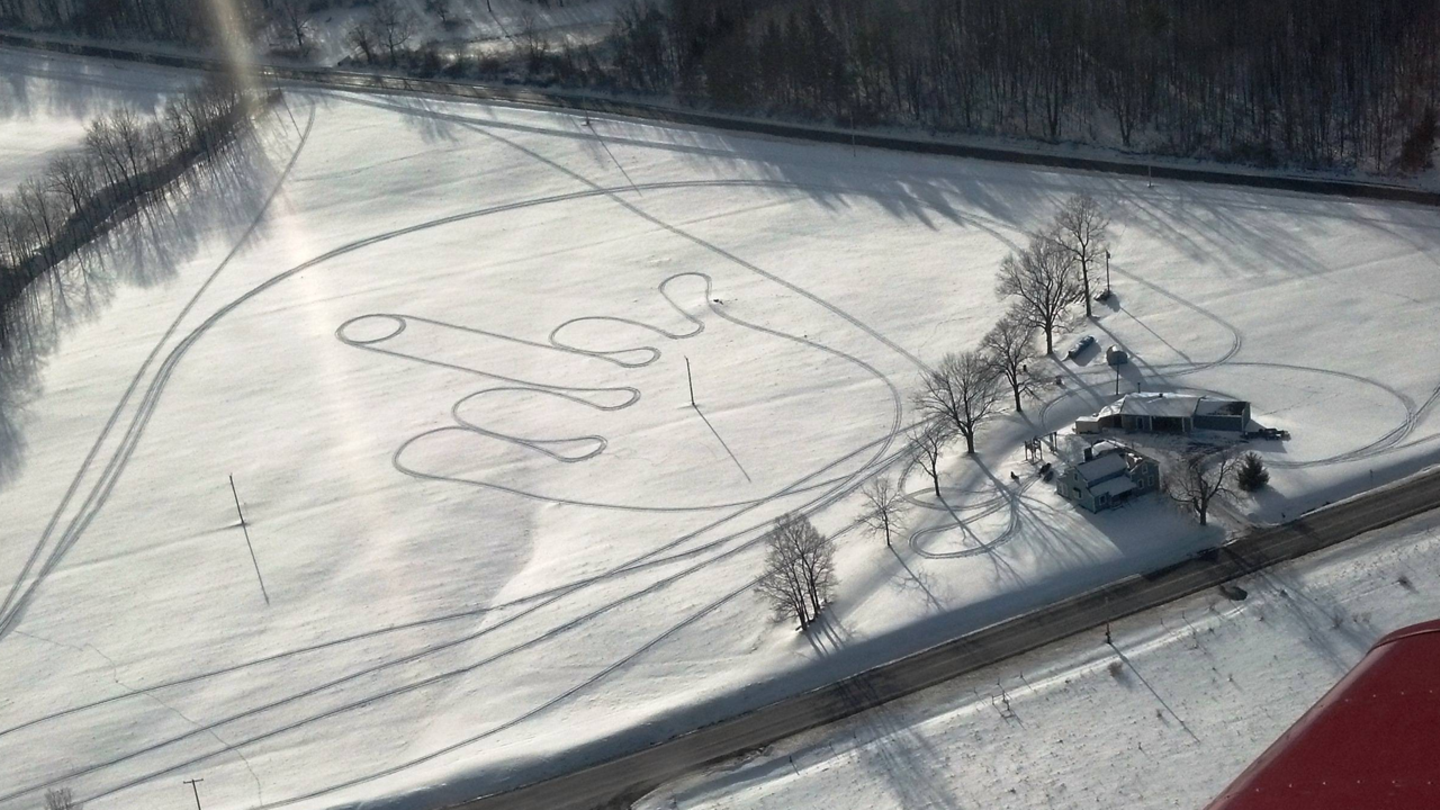 Luftaufnahme von Reifenspuren in Form eines Mittelfingers im Schnee