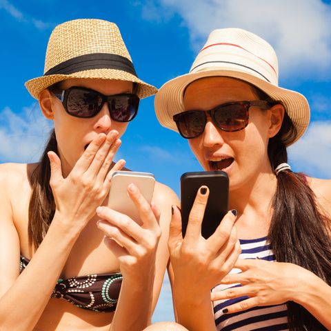 O2-Drosselung: Zwei Frauen in Strand-Kleidung schauen geschockt auf ihr Smartphone