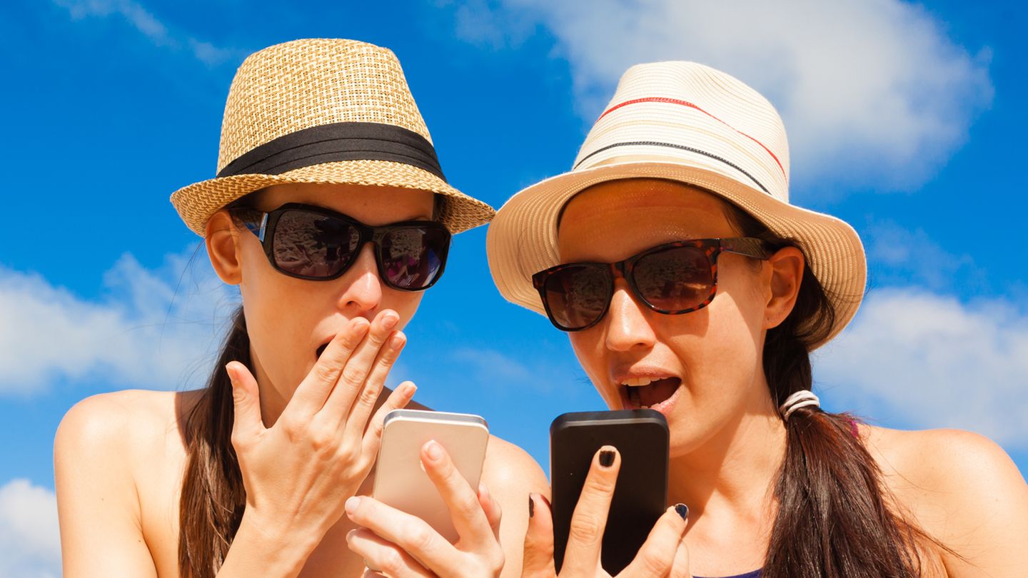 O2-Drosselung: Zwei Frauen in Strand-Kleidung schauen geschockt auf ihr Smartphone