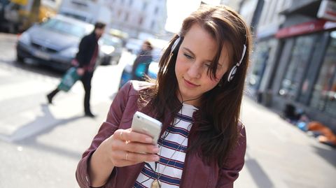 Eine junge Frau läuft über die Straße, während sie auf ihrem Handy schreibt