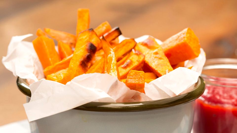 Süßkartoffel-Pommes in einer Schale. Daneben steht ein Glas mit Ketchup. Süßkartoffel-Pommes in einer Schale. Daneben steht ein Glas mit Ketchup.