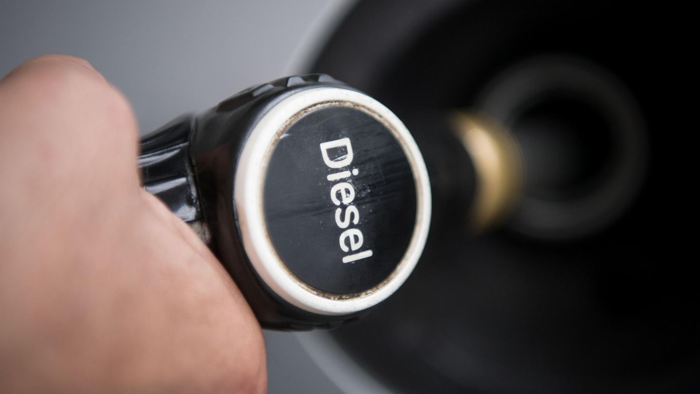 Ein Hand hält einen Tankrüssel mit der Aufschrift "Diesel" in den Tankstutzen eines silbergrauen Autos