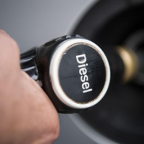 Ein Hand hält einen Tankrüssel mit der Aufschrift "Diesel" in den Tankstutzen eines silbergrauen Autos