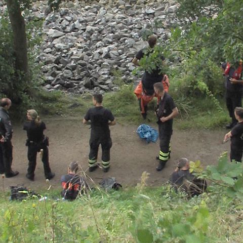 Polizisten und Feuerwehrleute bewachen einen blauen Sack, nachdem ein Angler Leichenteile am Elbufer gefunden hatte