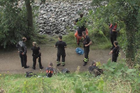 Polizisten und Feuerwehrleute bewachen einen blauen Sack, nachdem ein Angler Leichenteile am Elbufer gefunden hatte