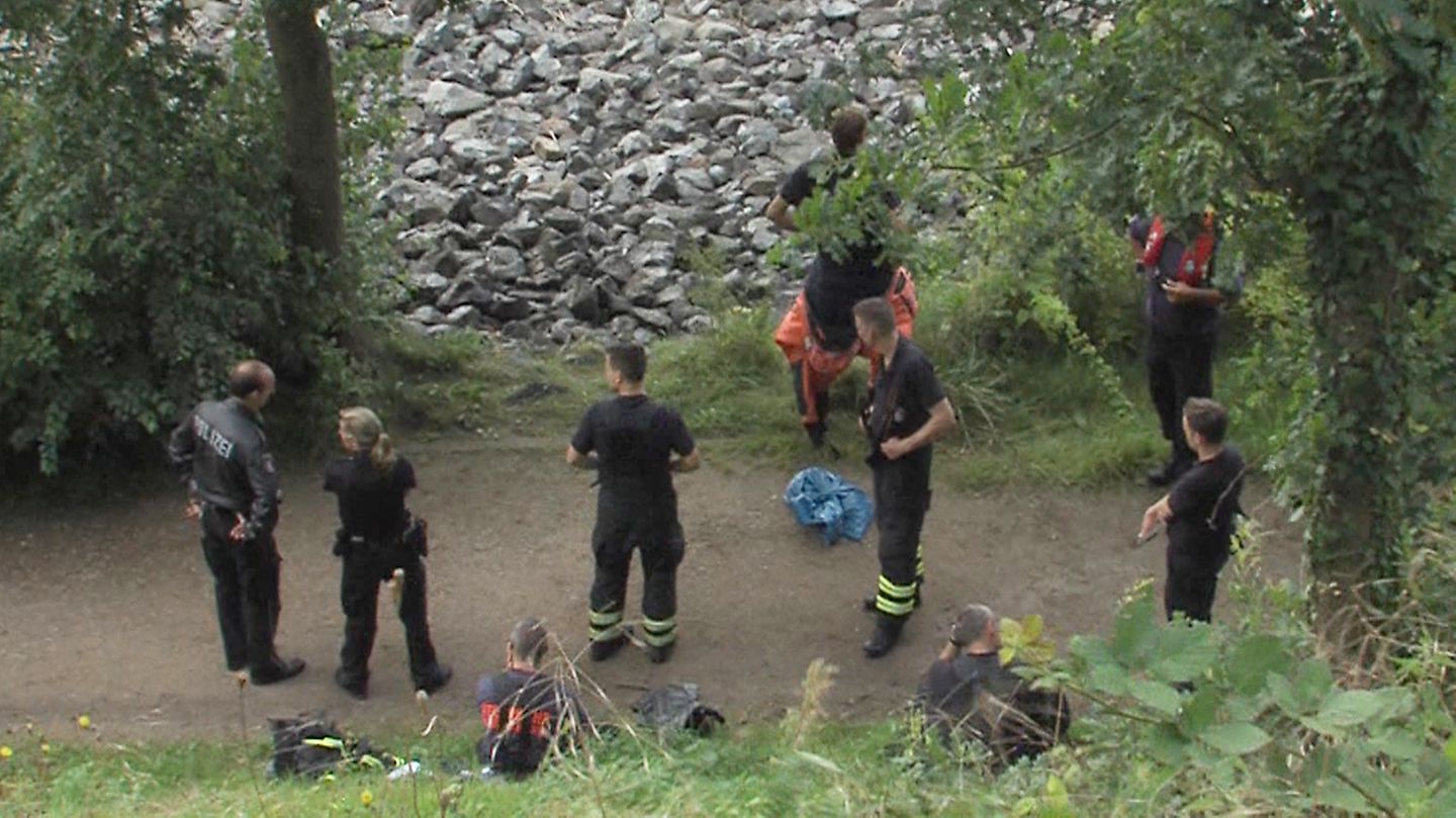 Polizisten und Feuerwehrleute bewachen einen blauen Sack, nachdem ein Angler Leichenteile am Elbufer gefunden hatte
