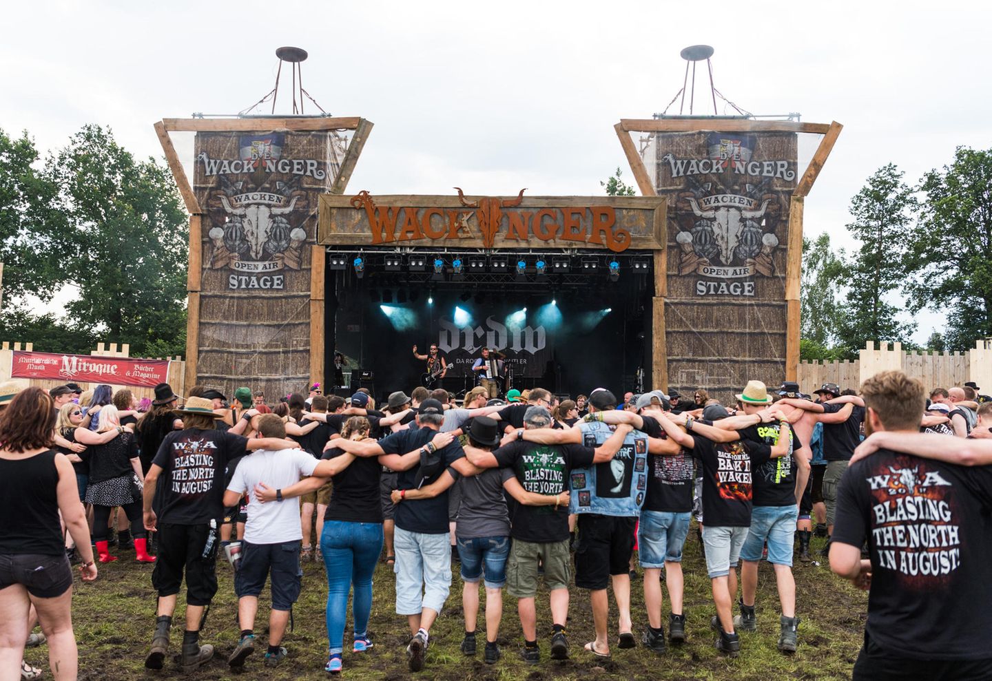 Festivalbesucher tanzen, Arm in Arm, auf dem Festivalgelände vor der Wackinger Stage