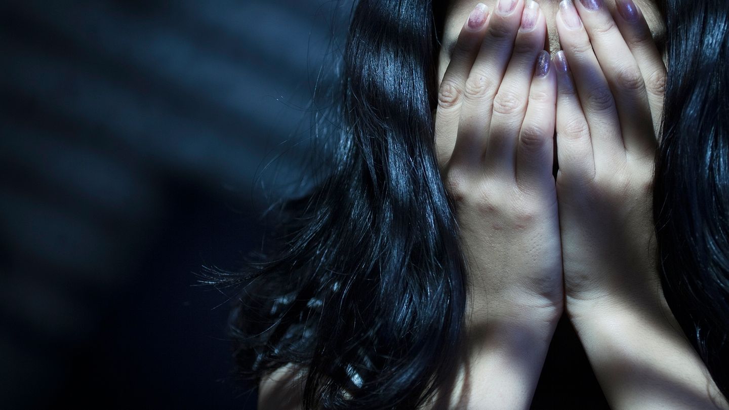 Dunkelhaarige Frau bedeckt ihr Gesicht mit beiden Händen