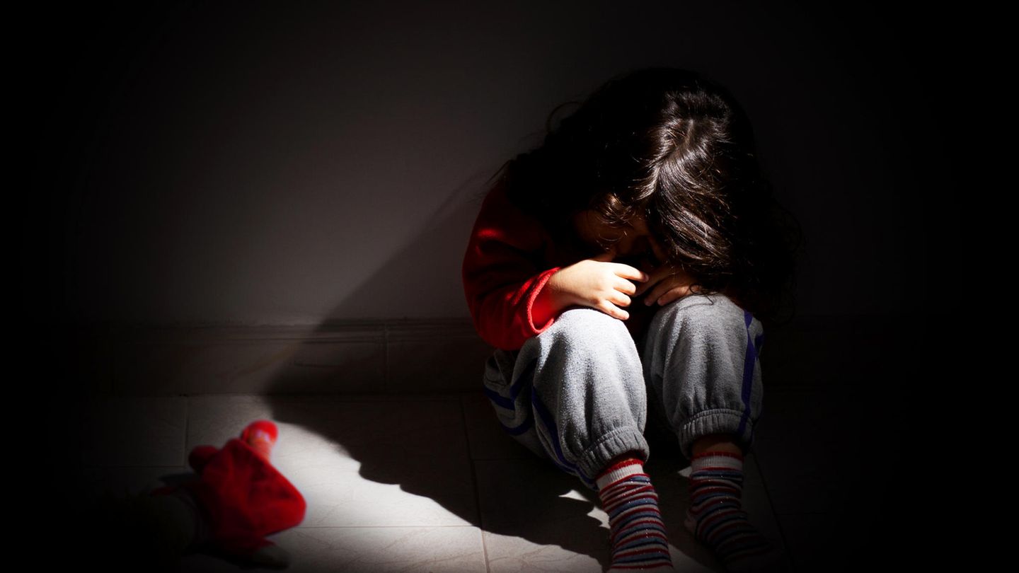 Ein Mädchen sitzt traurig im dunklen Zimmer