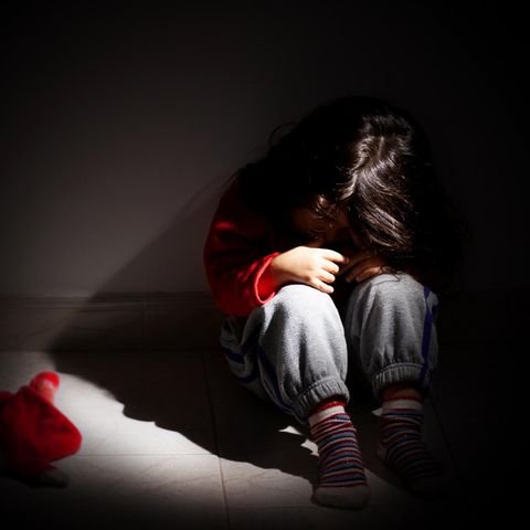 Ein Mädchen sitzt traurig im dunklen Zimmer
