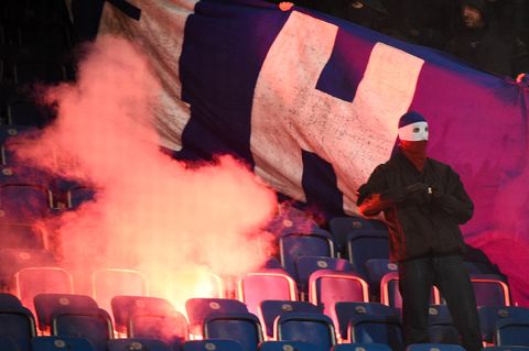 Vermummter Hooligan vor brennendem Banner von Hertha BSC auf den Rängen des Ostsee-Stadions in Berlin