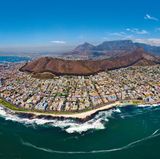 Aus der Möwenperspektive: Die Ausläufer von Kapstadt mit dem braunen Signal Hill in Bildmitte. Ganz links ist das Fußballstadion der Weltmeisterschaft von 2010 zu sehen.