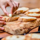 Sobald die Brothälften geröstet sind, reiben Sie jedes Stück mit der Knoblauchzehe ein. Das Brot wirkt dabei wie Schmirgelpapier.