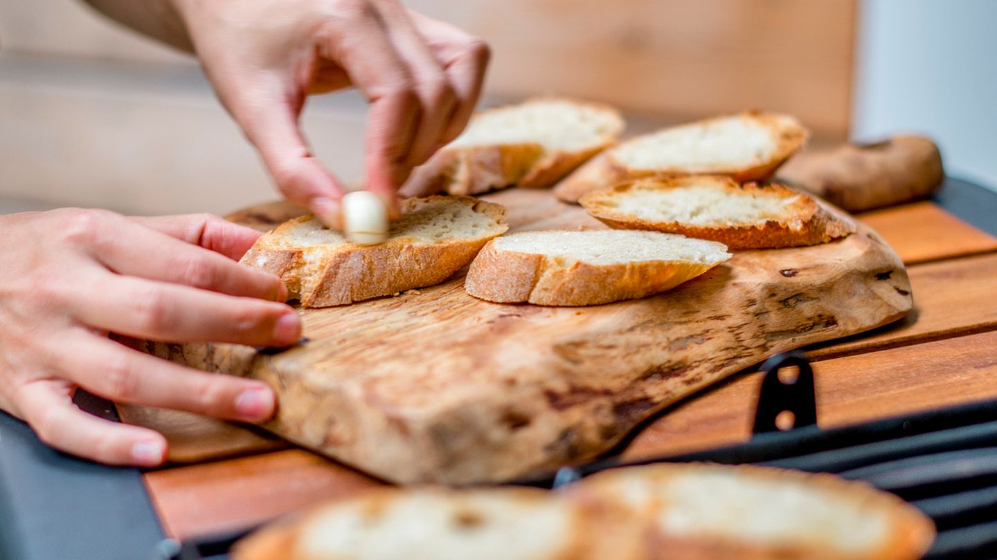 Sobald die Brothälften geröstet sind, reiben Sie jedes Stück mit der Knoblauchzehe ein. Das Brot wirkt dabei wie Schmirgelpapier.