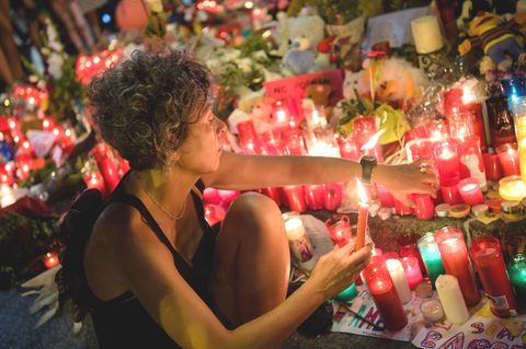 Eine Frau zündet am Anschlagsort auf der Flaniermeile Las Ramblas in Barcelona erloschene Kerzen wieder an