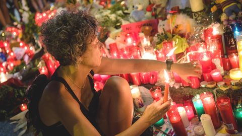 Eine Frau zündet am Anschlagsort auf der Flaniermeile Las Ramblas in Barcelona erloschene Kerzen wieder an