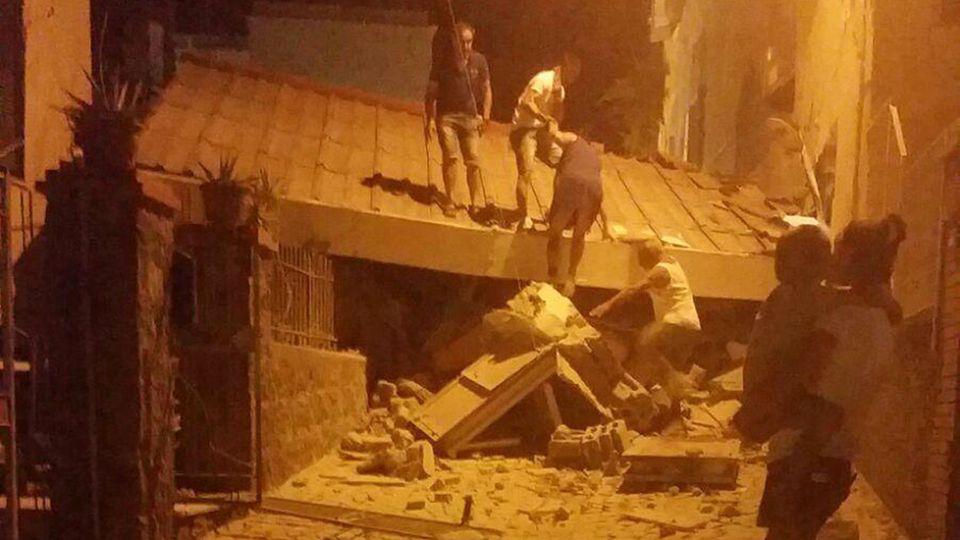 Erdbeben auf Ischia in Italien: Eine Frau steht mit einem Kleinkind im Arm vor einem eingestürzten Gebäude