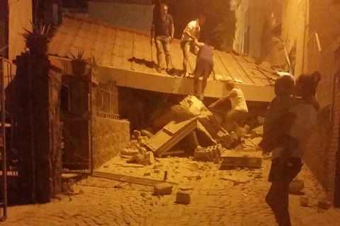 Erdbeben auf Ischia in Italien: Eine Frau steht mit einem Kleinkind im Arm vor einem eingestürzten Gebäude