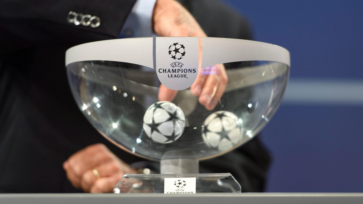 Eine Hand greift in einen durchsichtigen Lostopf mit Champions League Logo. In der Schale liegen noch zwei Kugeln.