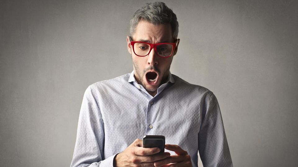Ein Mann schaut schockiert auf sein Smartphone