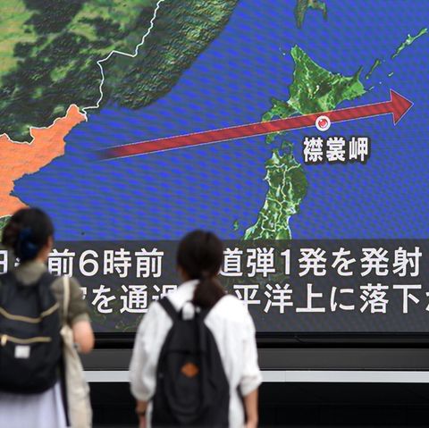Zwei Frauen in Tokio schauen auf einen Riesen-Bildschirm. Darauf ist eine Karte Japans zu sehen mit der Flugbahn der Rakete
