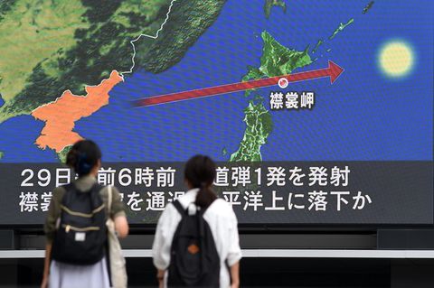 Zwei Frauen in Tokio schauen auf einen Riesen-Bildschirm. Darauf ist eine Karte Japans zu sehen mit der Flugbahn der Rakete
