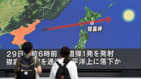 Zwei Frauen in Tokio schauen auf einen Riesen-Bildschirm. Darauf ist eine Karte Japans zu sehen mit der Flugbahn der Rakete
