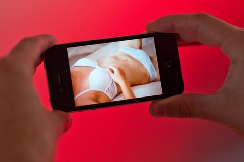Auf einem Smartphone-Display ist eine Frau zu sehen, die in weißer Unterwäsche auf einem Bett liegt