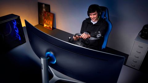 Ein junger Man spielt mit einem Lenkrad auf dem Samsung CHG90 Monitor