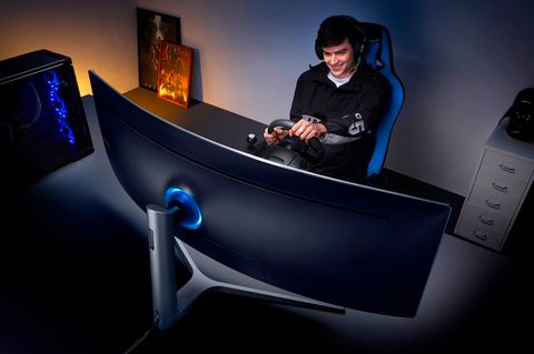 Ein junger Man spielt mit einem Lenkrad auf dem Samsung CHG90 Monitor