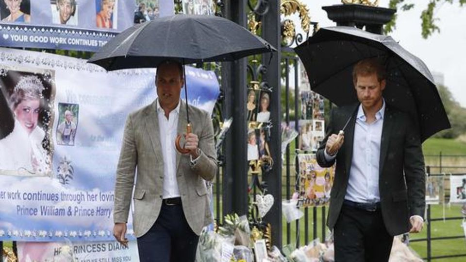 William und Harry schauen sich vor dem Kensington Palast niedergelegte Blumen an