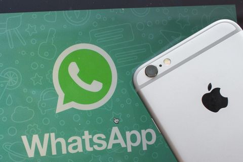 Ein iPhone liegt neben einem Bildschirm mit dem Whatsapp-Logo