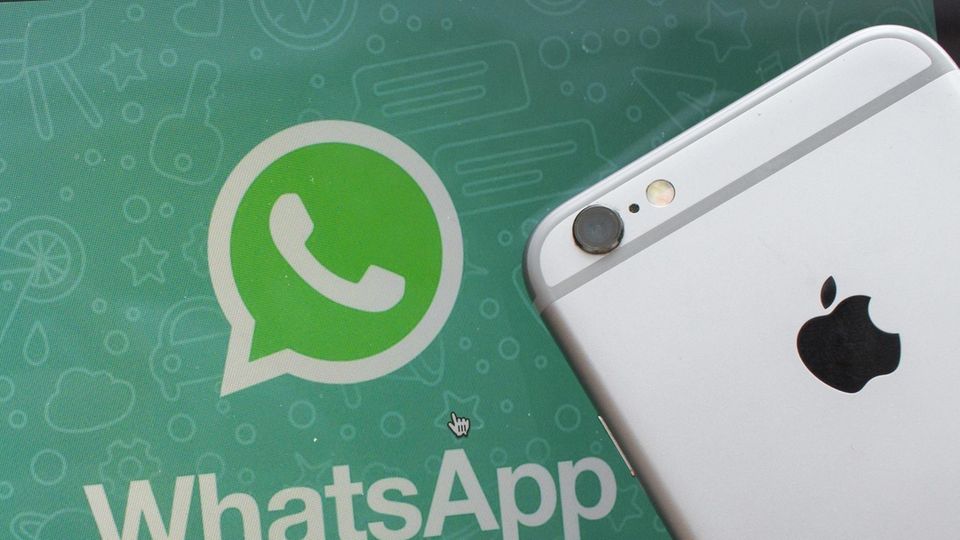 Ein iPhone liegt neben einem Bildschirm mit dem Whatsapp-Logo