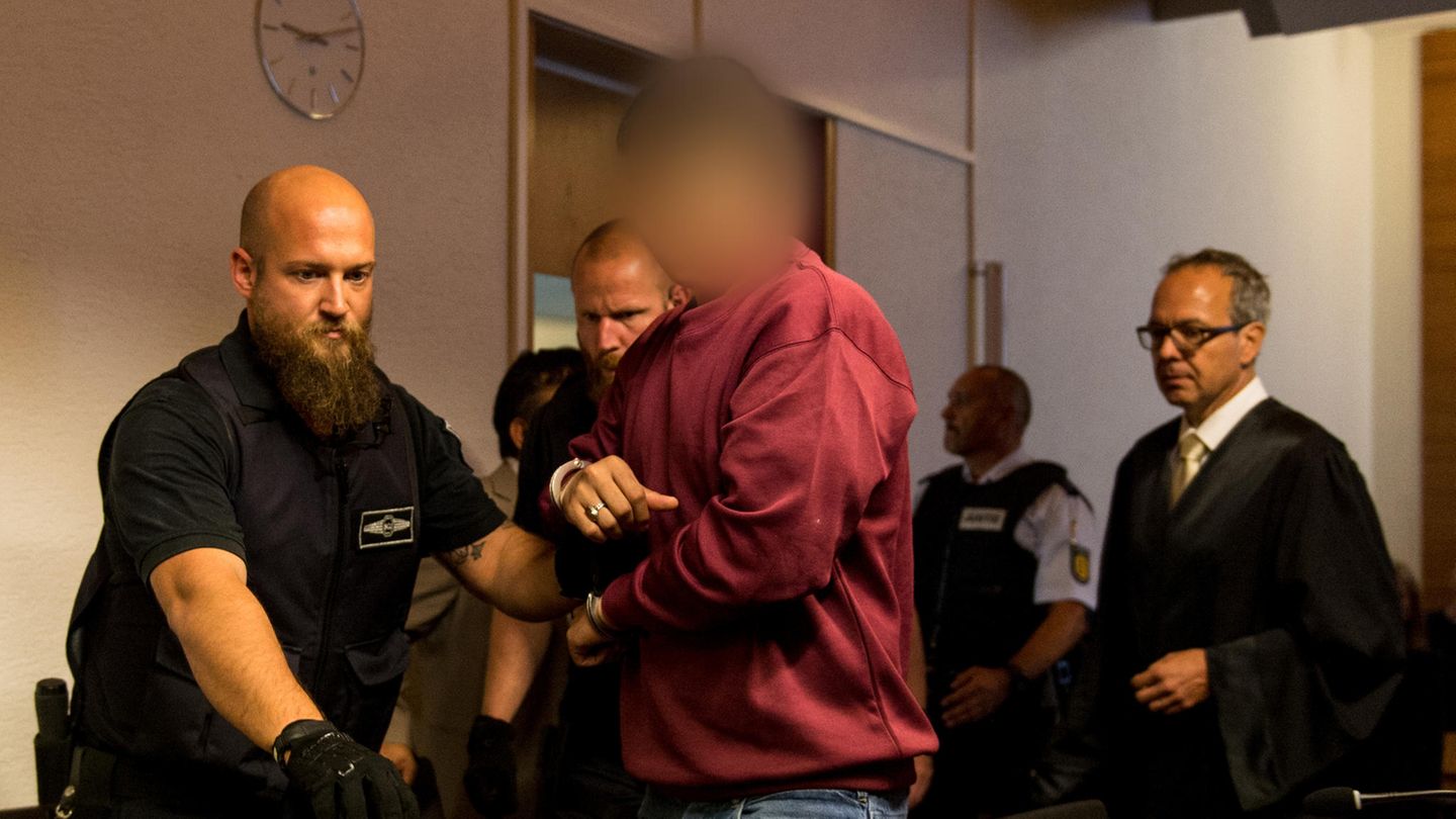 Hussein K. trägt ein weinrotes Sweatshirt, als er in Handschellen von Justizbeamten in den Gerichtssaal in Freiburg geführt wird