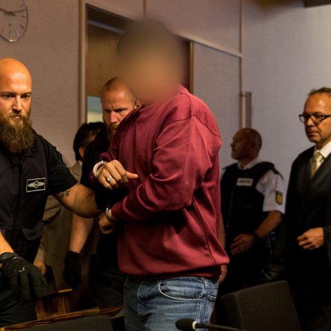 Hussein K. trägt ein weinrotes Sweatshirt, als er in Handschellen von Justizbeamten in den Gerichtssaal in Freiburg geführt wird