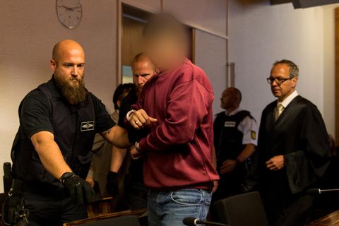 Hussein K. trägt ein weinrotes Sweatshirt, als er in Handschellen von Justizbeamten in den Gerichtssaal in Freiburg geführt wird