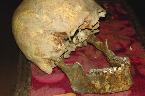 Auf einem roten Tuch liegt ein alter Schädel. Der Unterkiefer ist aufgeklappt, dem Schädel fehlen die Augenhöhlen