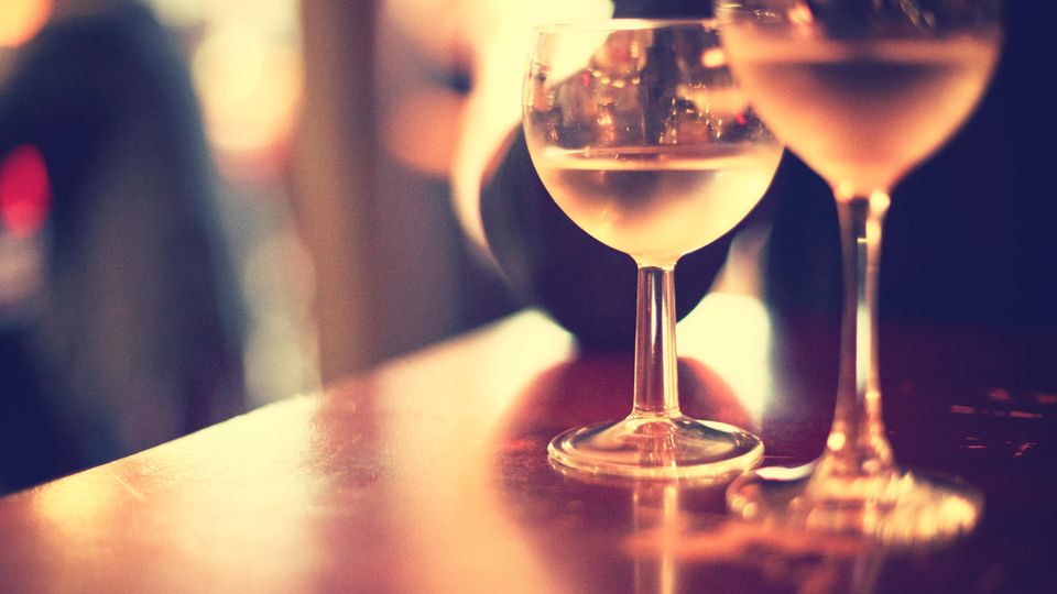Zwei Weingläser stehen im gelbem Lichtschein einer Bar