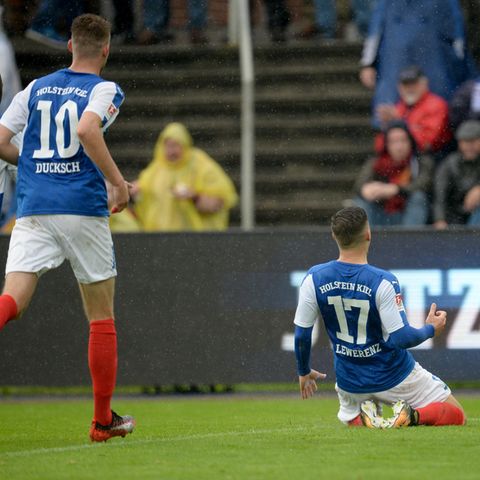 Der Kieler Torschütze Lewerenz rutscht nach seinem Treffer auf Knien Richtung Fans, zwei Mitspieler laufen hinterher