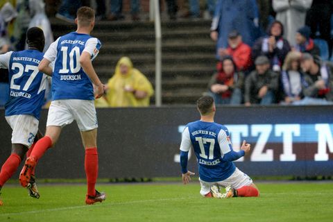 Der Kieler Torschütze Lewerenz rutscht nach seinem Treffer auf Knien Richtung Fans, zwei Mitspieler laufen hinterher