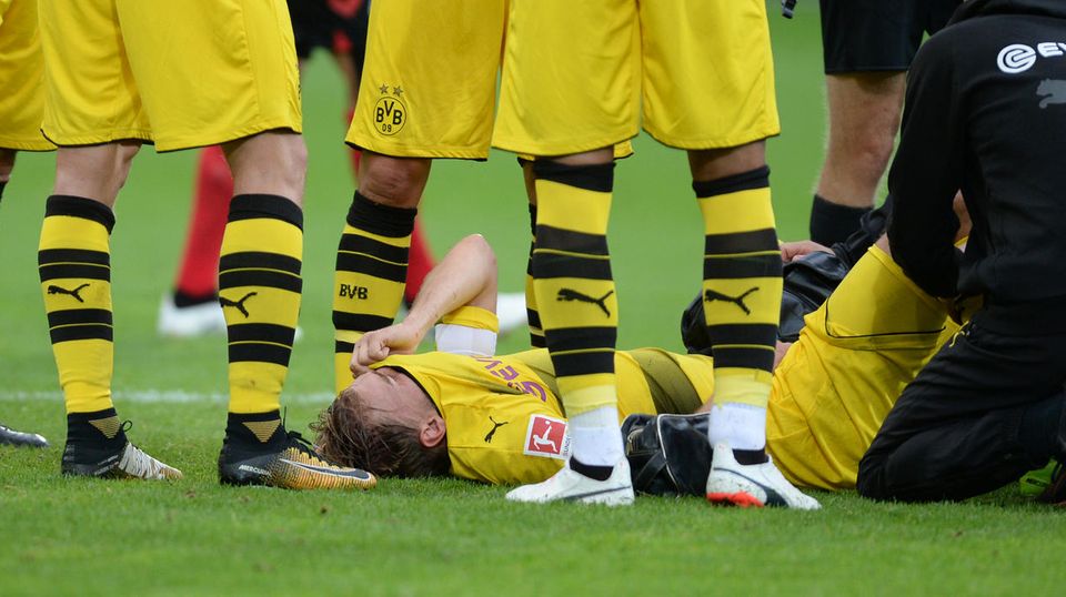 Marcel Schmelzer BVB verletzt Marcel Schmelzer liegt rücklings auf dem Rasen, das gelbe BVB-Trikot vor das Gesicht gezogen. Zwei Betreuer knien bei ihm