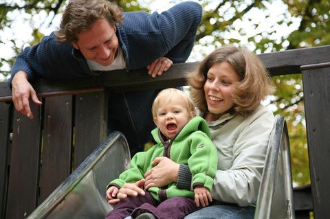 Junge Familie mit Kind auf der Spielplatz-Rutsche
